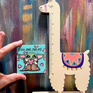 May include: A small square canvas painting featuring a cartoon character holding a heart, with the text "YODA ONE FOR ME". A wooden llama-shaped ruler stands next to the painting. The ruler has a colorful design on its back and measures up to 6 inches.