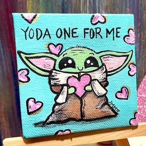 May include: A small square canvas painting featuring a green alien-like character holding a pink heart. The text "YODA ONE FOR ME" is written above the character. Pink hearts are scattered around the image. The painting is displayed on a small wooden easel.