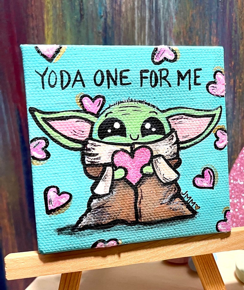 May include: A small square canvas painting featuring a green alien-like character holding a pink heart. The text "YODA ONE FOR ME" is written above the character. Pink hearts are scattered around the image. The painting is displayed on a small wooden easel.