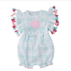May include: A light blue and white plaid baby romper with pink and blue tassels on the sleeves. The romper has a bow at the waist and is monogrammed with the letters "EPC".
