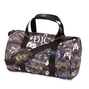 May include: A black duffel bag with a camouflage pattern featuring video game controllers. The bag has a black zipper and a white monogram that reads "DJC".