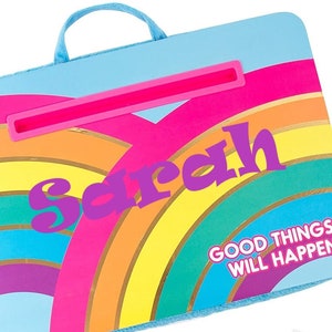 May include: A blue and rainbow-colored lap desk with a handle and a built-in tablet stand. The desk has the name "Sarah" and the phrase "Good things will happen" printed on it.