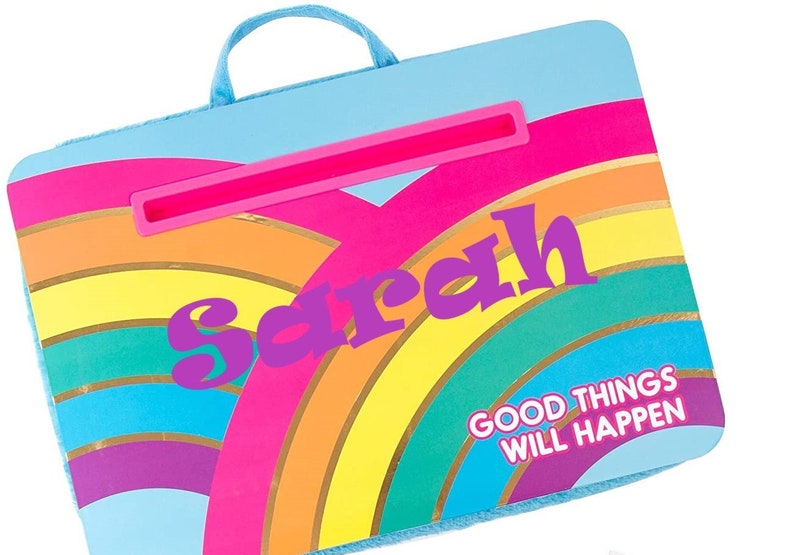 May include: A blue and rainbow-colored lap desk with a handle and a built-in tablet stand. The desk has the name "Sarah" and the phrase "Good things will happen" printed on it.