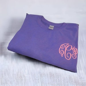 May include: A purple t-shirt with a pink monogram of the letters "PS" embroidered on the front.