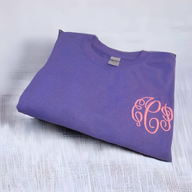 May include: A purple t-shirt with a pink monogram of the letters "PS" embroidered on the front.