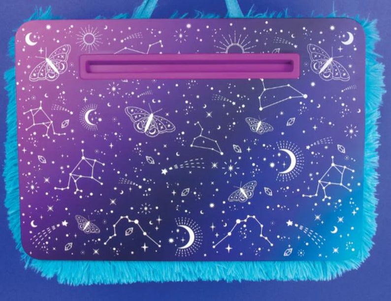 May include: A purple and blue laptop stand with a white fuzzy trim. The stand has a white design of stars, constellations, and butterflies.