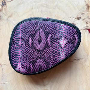 May include: A pink and black snakeskin-patterned clutch purse with a black trim.