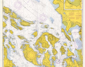 May include: A nautical chart of the Strait of Juan de Fuca and the Strait of Georgia, showing the islands and waterways of the region. The chart is printed in black and white with yellow and blue highlights. The chart includes compass roses, depth soundings, and navigational aids.