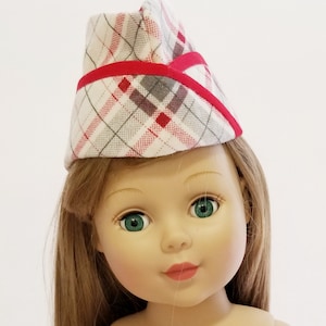 May include: A doll wearing a red and white plaid hat with a red trim. The hat has a pointed top and is angled slightly to the side. The doll has long brown hair and green eyes.