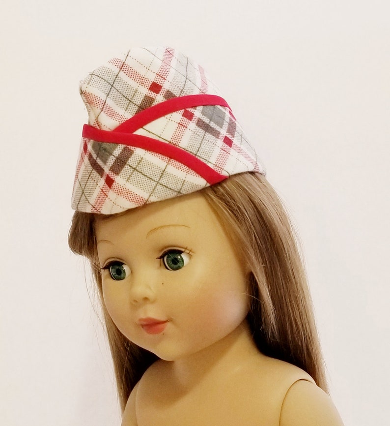 K&ouml;nnte beinhalten: Eine Puppe tr&auml;gt einen roten und wei&szlig;en karierten Hut mit rotem Besatz. Der Hut hat eine spitze Oberseite und ist leicht zur Seite geneigt. Die Puppe hat langes braunes Haar und gr&uuml;ne Augen.