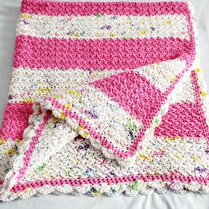 May include: A handmade crochet blanket featuring alternating horizontal stripes of solid hot pink yarn and white yarn speckled with multicolored flecks. The blanket has a textured stitch pattern and a scalloped white crochet border edge.