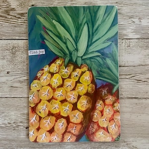 May include: A rectangular notebook with a vibrant pineapple painting. The artwork features a detailed depiction of two pineapples in shades of yellow, orange, and red, with green leaves. The words "find joy" are in a small white rectangle.