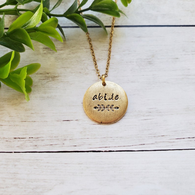 May include: Gold necklace with a round pendant that says "abide" with a small leaf design.
