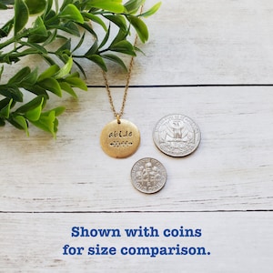 May include: Gold necklace with a round pendant that says "abide" with a small leaf design. The pendant is shown next to UK coins for size comparison.