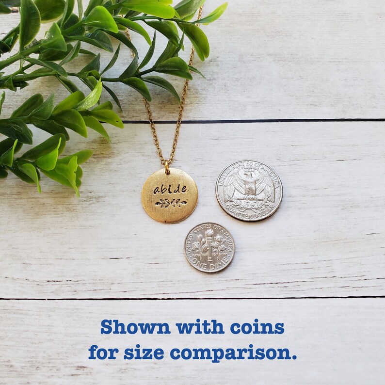 May include: Gold necklace with a round pendant that says "abide" with a small leaf design. The pendant is shown next to UK coins for size comparison.