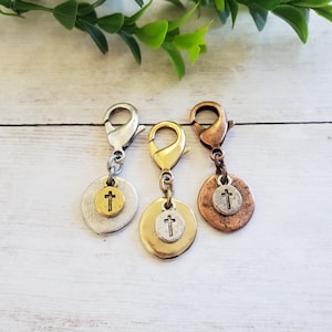 May include: Three metal charms with cross pendants. Each charm has a different finish: silver, gold, and copper. The charms are attached to lobster claw clasps, ready to be added to a necklace or bracelet.