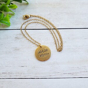 May include: Gold necklace with a round pendant that says "abide" with a small leaf design underneath the word.