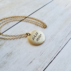 May include: Gold necklace with a round pendant that says "abide" with a small leaf design.