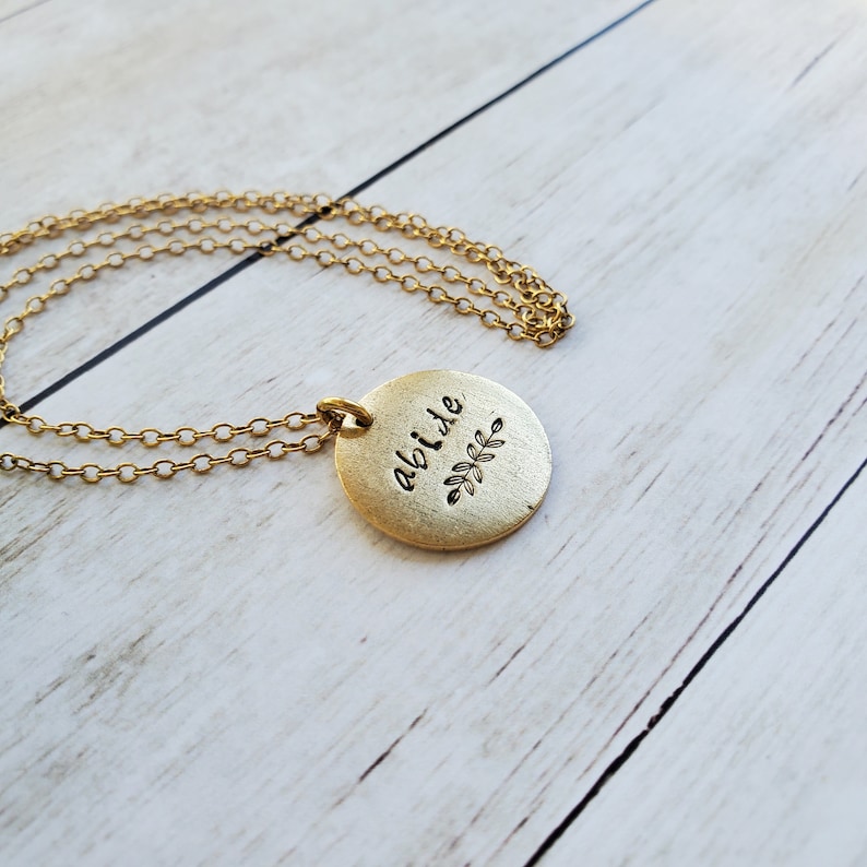 May include: Gold necklace with a round pendant that says "abide" with a small leaf design.