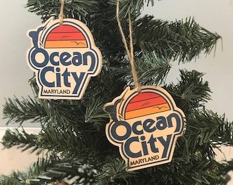 May include: Two wooden Christmas decorations featuring a retro sunset design and the text "Ocean City Maryland".