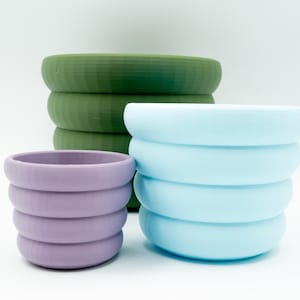 May include: Three stacked plant pots in different sizes. The largest pot is green, the middle pot is light blue, and the smallest pot is purple.