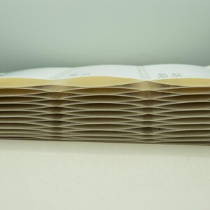 May include: A stack of white paper labels with a slightly yellowed tint. The labels are folded in a zig-zag pattern, creating a wave-like effect.