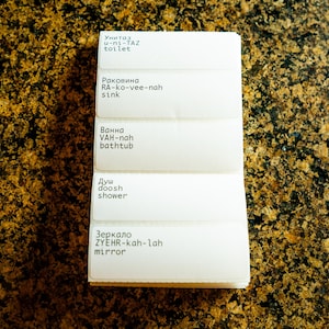 May include: White labels with Russian words and their English translations for bathroom items. The labels include: toilet, sink, bathtub, shower, and mirror.
