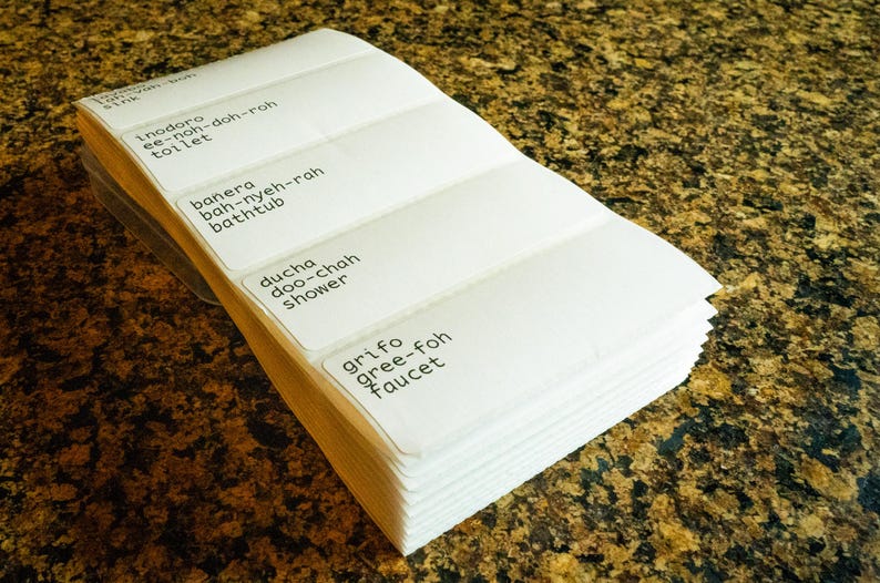 May include: A stack of white labels with black text. The labels are for bathroom items and include the words "Inodoro", "Banera", "Ducha", and "Grifo".