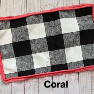 Puede incluir: Una tela de cuadros negros y blancos con un borde de color coral. La tela está sobre una superficie de madera. La palabra "Coral" está escrita debajo de la tela.
