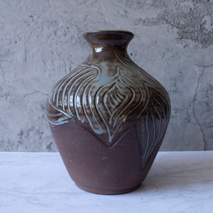May include: A brown ceramic vase with a light blue glaze and a leaf design.