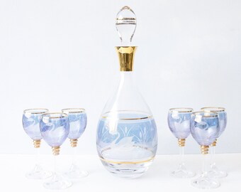 May include: A set of six blue glass decanter and glasses with gold trim. The decanter has a swan design etched into the glass. The glasses are small and have a similar design.