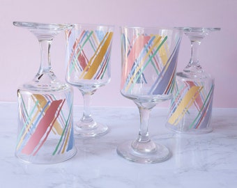 May include: Set of four clear glass wine glasses with a colorful geometric pattern. The pattern features diagonal lines in shades of pink, yellow, blue, and green.