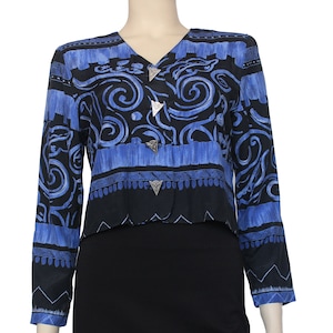 May include: A blue and black patterned cropped jacket with silver triangular buttons. The jacket has a V-neck and long sleeves.