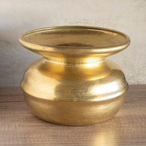 May include: A gold-colored metal vase with a round, wide base and a slightly flared top. The vase has a textured, crackled finish.
