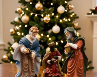 May include: Three ceramic figurines depicting the Three Wise Men. The left figure wears a blue robe, the center figure wears a red robe and holds a small chest, and the right figure wears a green cloak over a red robe while holding a lantern.