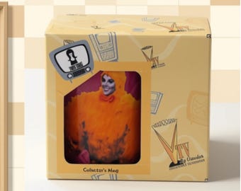 May include: A rectangular cardboard box with a light yellow background featuring a cutout window displaying a mug with an orange character graphic. The box includes a television icon, the text Collector's Mug, and VTV branding with line art illustrations.