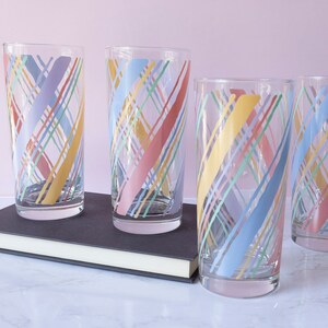 May include: Set of four clear glass tumblers with a colorful geometric pattern. The pattern features diagonal lines in shades of pink, blue, yellow, and green.