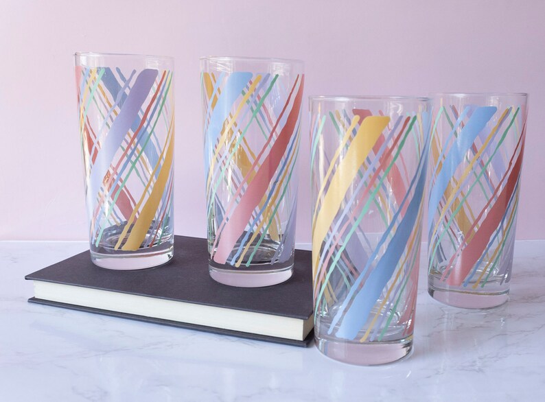 May include: Set of four clear glass tumblers with a colorful geometric pattern. The pattern features diagonal lines in shades of pink, blue, yellow, and green.