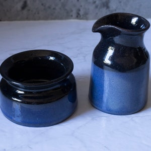 May include: A set of two blue and black ceramic kitchenware pieces. A small pitcher and a round bowl with a wide rim.