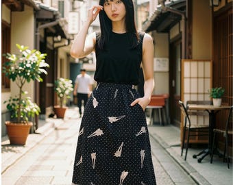 May include: A black sleeveless top paired with a black midi skirt featuring a white polka dot pattern and light pink hair accessory motifs. The skirt has a high waist, a flared silhouette, and side pockets, creating a cohesive ensemble.