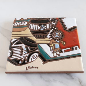 May include: A ceramic tile with a Southwestern design featuring a Native American figure, a pot, and geometric patterns in shades of brown, white, blue, green, and red. The tile is signed "Kushner".