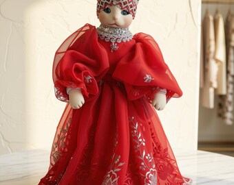 May include: A cat-faced doll wearing a vibrant red sheer gown with voluminous sleeves and intricate silver floral embroidery. The doll features a matching red and silver crown-like headpiece and a silver collar, presenting a regal appearance.