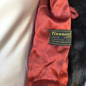 Puede incluir: Primer plano de un forro de tela rojo con una etiqueta negra que dice "tissavel France Genuine French Simulation Fur. Treat and clean like fur."