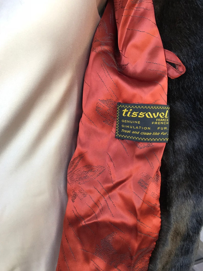 Puede incluir: Primer plano de un forro de tela rojo con una etiqueta negra que dice "tissavel France Genuine French Simulation Fur. Treat and clean like fur."