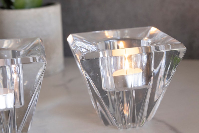May include: Two clear glass candle holders with a geometric design. The candle holders are filled with tea lights that are lit.