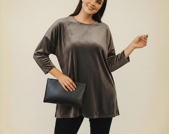 May include: A long-sleeved, crew-neck top made of a grey velvet fabric with a subtle sheen, paired with solid black trousers and a smooth, rectangular black clutch bag held in front of the torso.