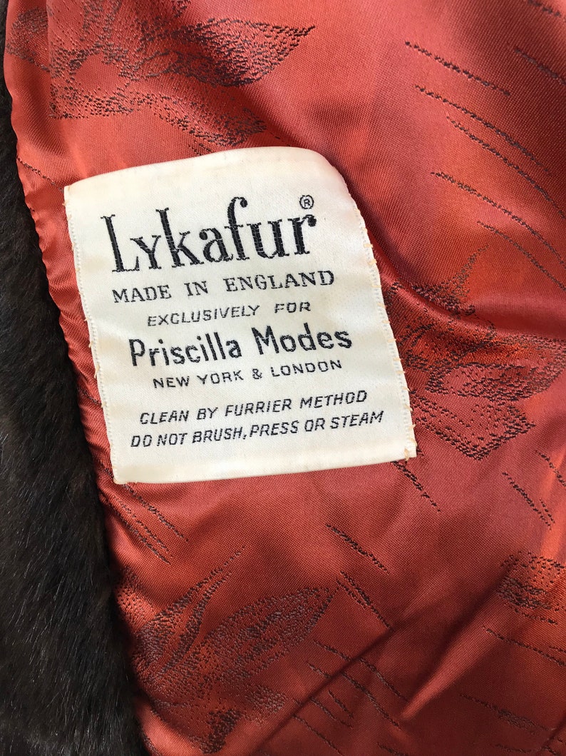 Puede incluir: Una etiqueta blanca con texto negro que dice "Lykafur Hecho en Inglaterra Exclusivamente para Priscilla Modes Nueva York & Londres Limpieza por m&eacute;todo de peletero No cepillar, presionar o vaporizar"