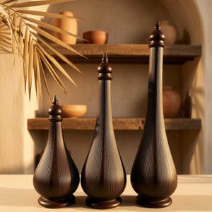 May include: Three dark brown decorative bottles of varying heights, each featuring a slender neck, a rounded base, a finial-style stopper, and a fine vertical ribbed texture across the entire surface of the dark wood-toned vessels.