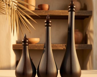 May include: Three dark brown decorative bottles of varying heights, each featuring a slender neck, a rounded base, a finial-style stopper, and a fine vertical ribbed texture across the entire surface of the dark wood-toned vessels.