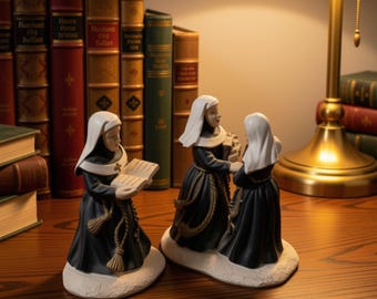 May include: Three ceramic nun figurines standing on white bases. One figurine holds an open book, while the other two interact. They wear black habits with white veils and rope belts with tassels. The figures are detailed with painted facial features.